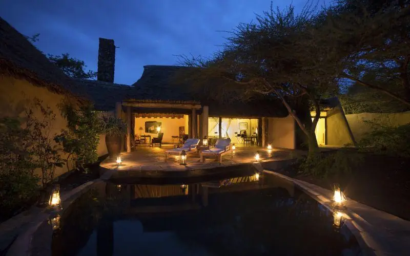 Illuminated lodge exterior with pool and lounge seating at dusk, Ol Donyo Lodge, Amboseli and Chyulu Hills, Kenya