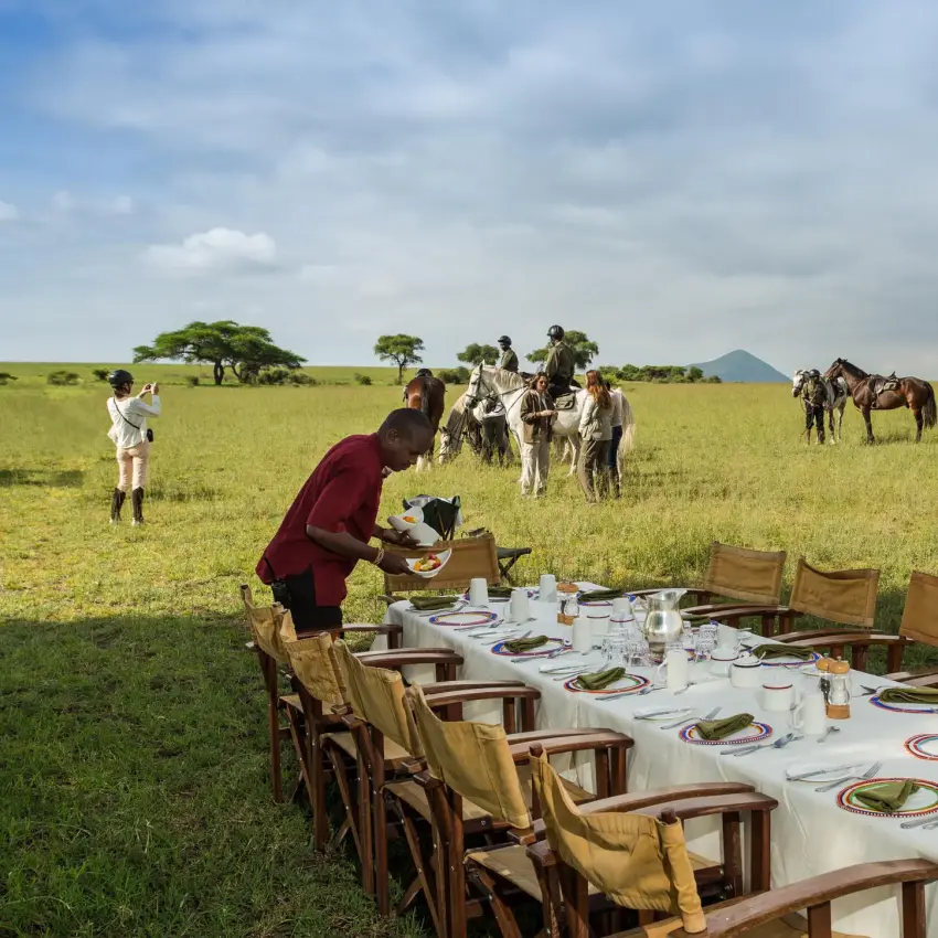 Outdoor dining setup in expansive savanna landscape with guests, Ol Donyo Lodge, Amboseli and Chyulu Hills, Kenya