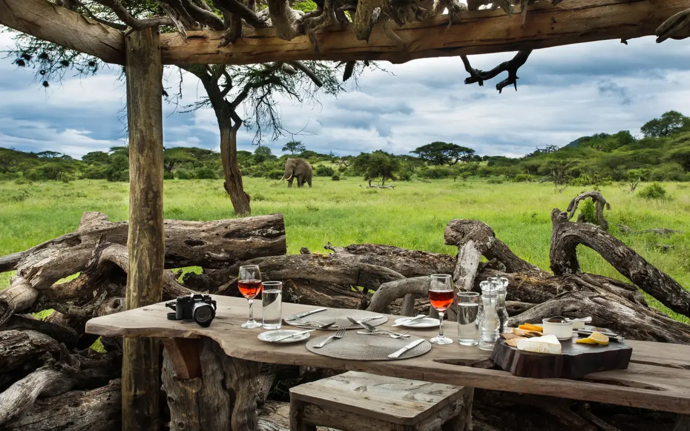 Outdoor dining table set with savanna wildlife visible beyond, Ol Donyo Lodge, Amboseli and Chyulu Hills, Kenya