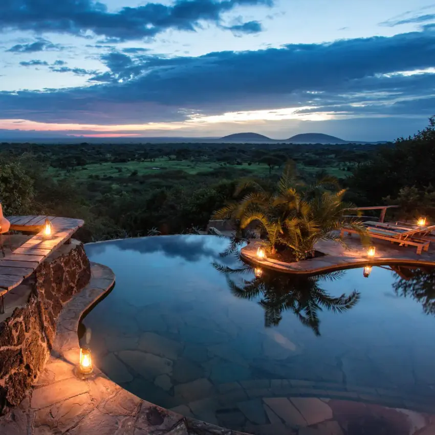 Candlelit deck overlooking savanna at twilight with pool, Amboseli and Chyulu Hills, Kenya