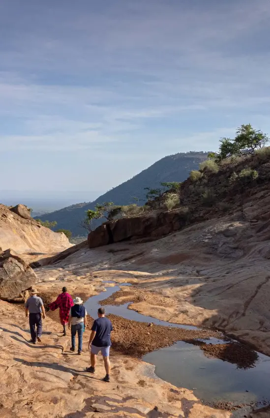 Guests hiking through rocky riverbed with mountain vista, Ol Lentille, Laikipia Highlands, Kenya