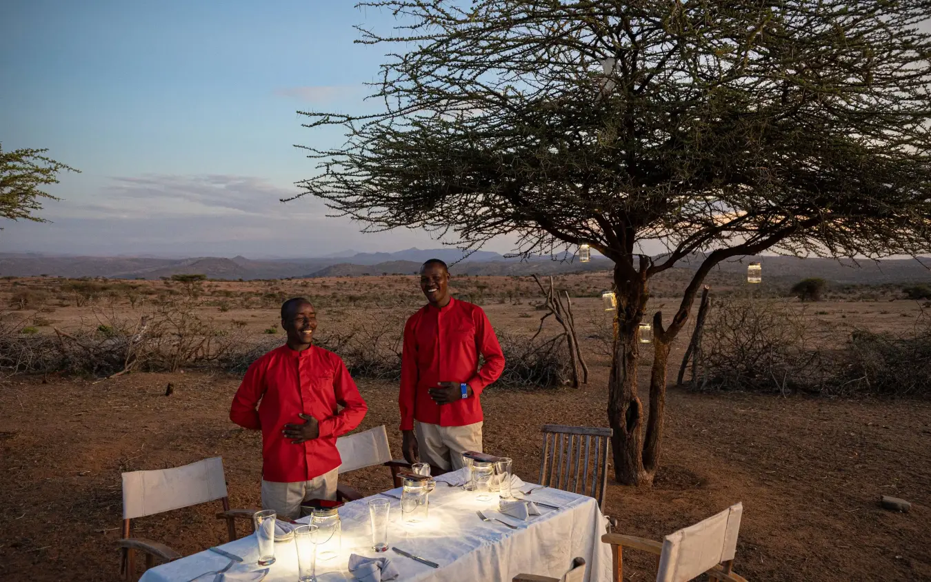 Staff setting elegant table under acacia tree at sunset, Ol Lentille, Laikipia Highlands, Kenya