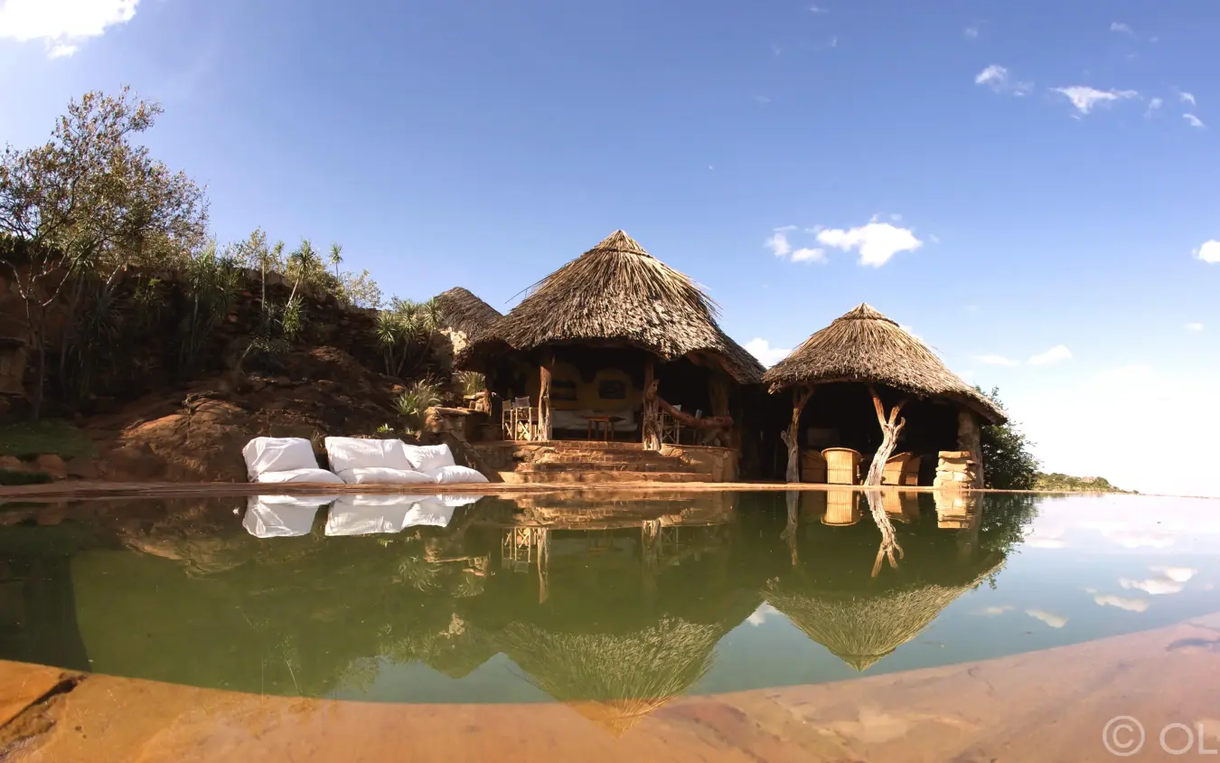 Thatched-roof structures reflected in calm waterhole, Ol Malo Lodge, Laikipia Highlands, Kenya