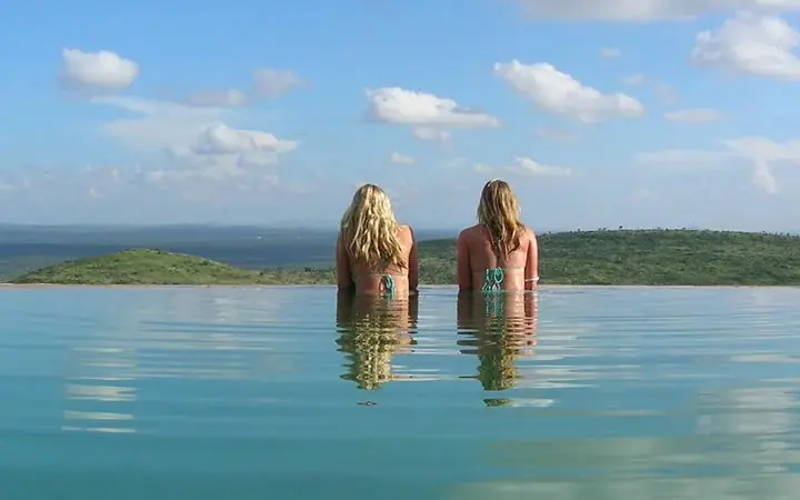 Two women in infinity pool overlooking savanna landscape, Ol Malo Lodge, Laikipia Highlands, Kenya