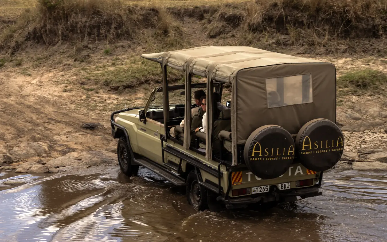 Safari vehicle crossing shallow river during game drive, Olakira Migration Camp, Serengeti National Park, Tanzania