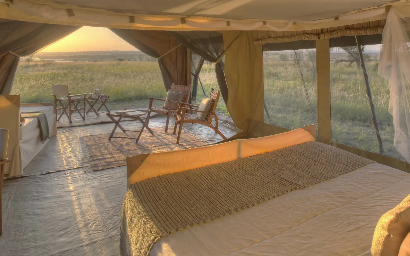 Luxury safari tent bedroom with open-air viewing deck overlooking grassland at sunset, Olakira Migration Camp, Serengeti National Park, Tanzania