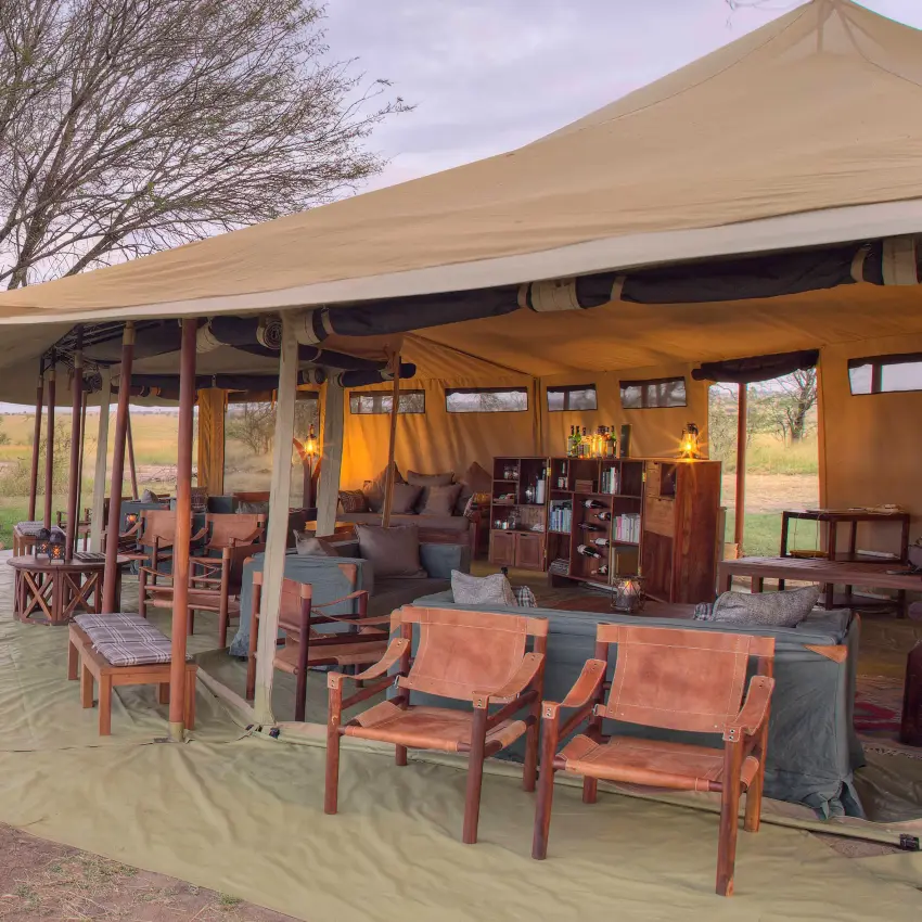 Safari tent lounge with seating and warm lighting at dusk, Olakira Migration Camp, Serengeti National Park, Tanzania