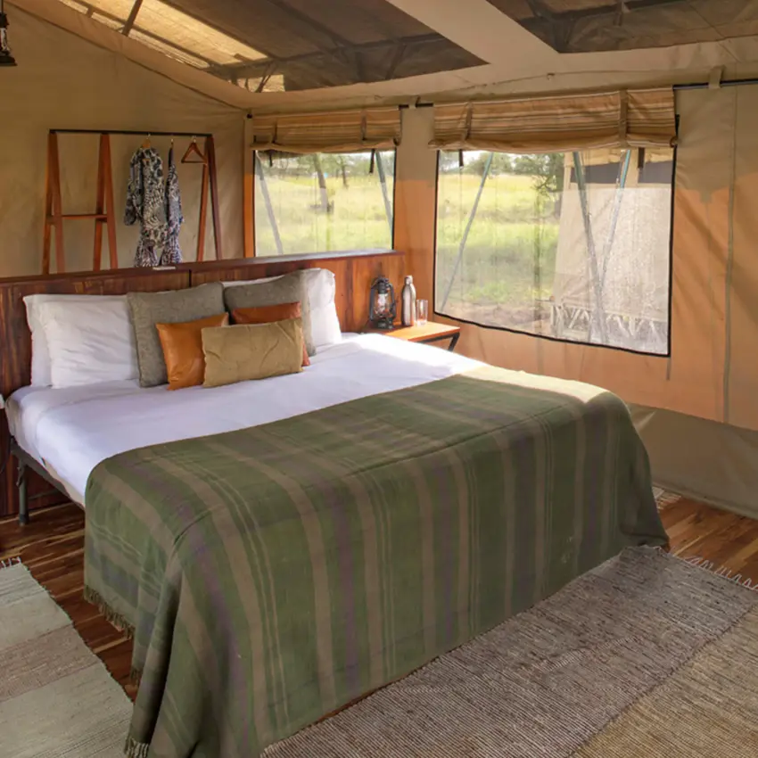 Canvas safari tent bedroom with wooden furnishings and large windows, Olakira Migration Camp, Serengeti National Park, Tanzania