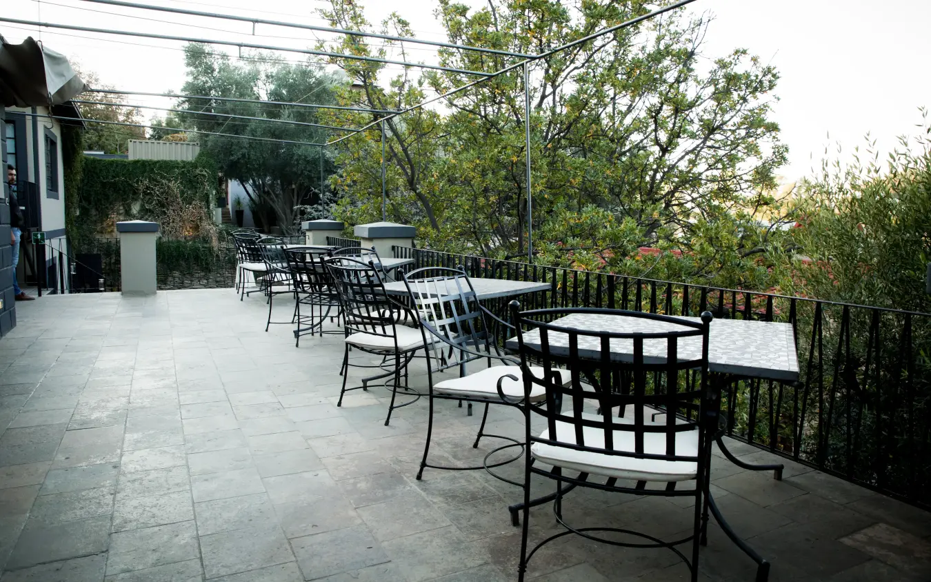 Outdoor terrace with metal furniture overlooking forested valley at dusk, Olive Grove Guesthouse, Windhoek, Namibia