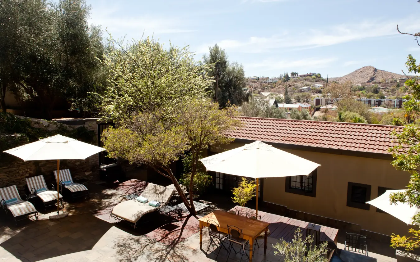 Courtyard terrace with shade umbrellas and olive trees overlooking hillside valley, Olive Grove Guesthouse, Windhoek, Namibia