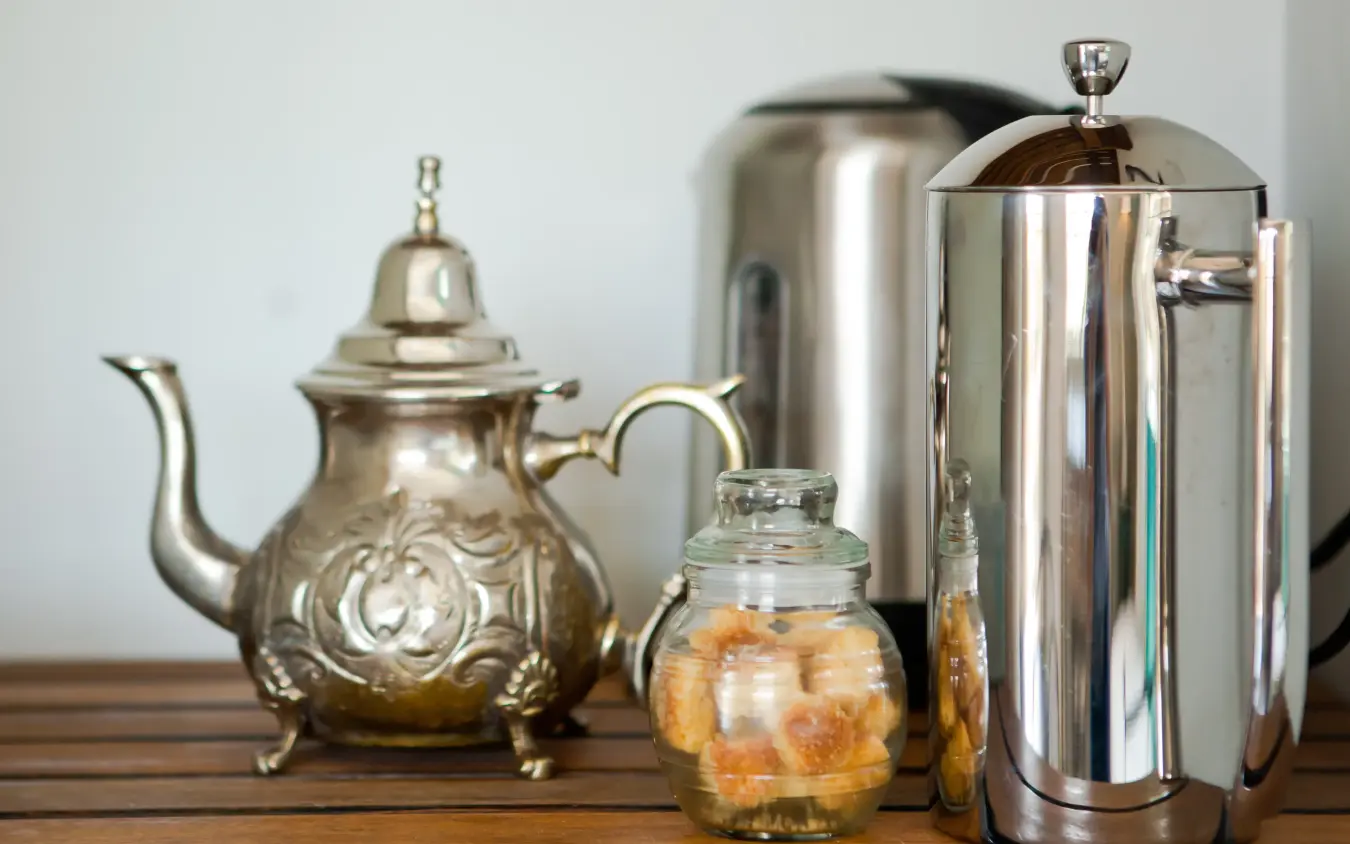 Tea service with ornate silver teapot and stainless steel pitcher on wooden table, Olive Grove Guesthouse, Windhoek, Namibia