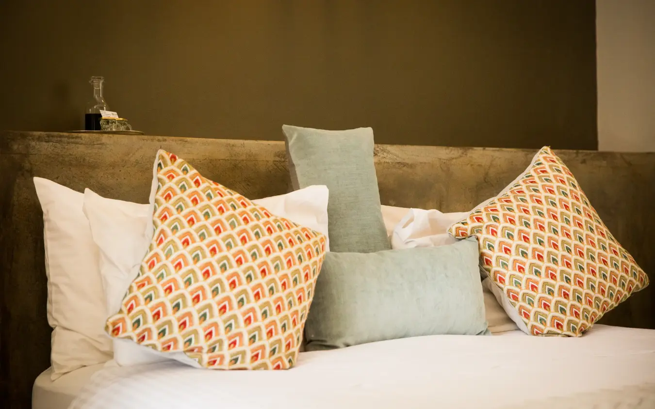 Bed with decorative patterned pillows against olive green wall, Olive Grove Guesthouse, Windhoek, Namibia