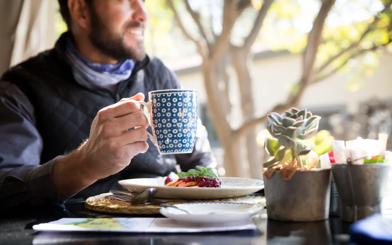 Man enjoying beverage at outdoor dining table with succulent plants, Olive Grove Guesthouse, Windhoek, Namibia