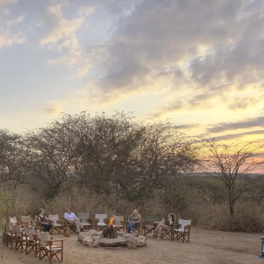 Guests gathered around campfire at sunset in savanna, Oliver’s Camp, Tarangire National Park, Tanzania