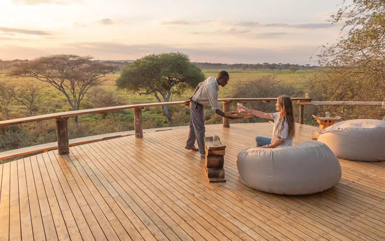 Guests relax on wooden deck overlooking savanna landscape, Oliver’s Camp, Tarangire National Park, Tanzania