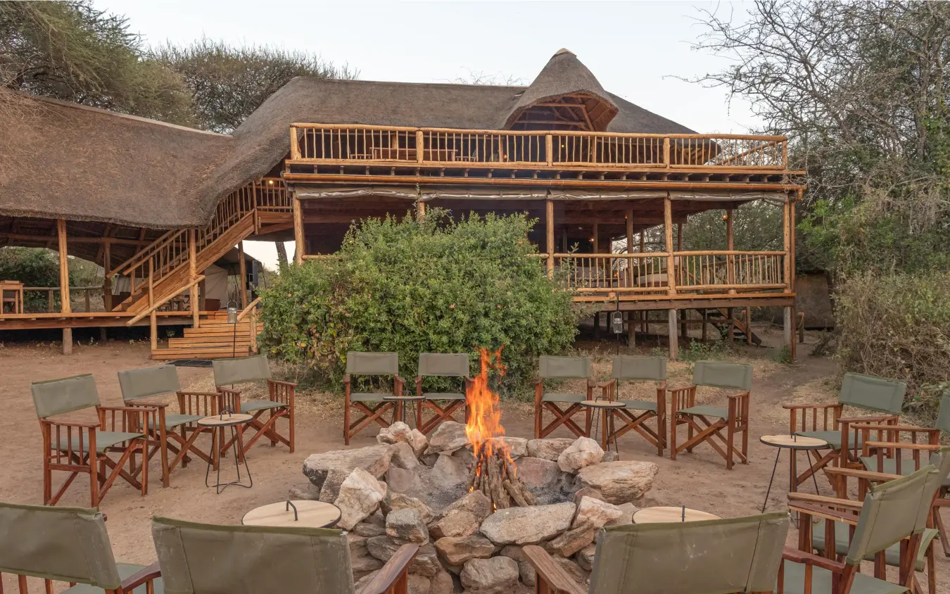 Thatched lodge building with firepit seating area at dusk, Oliver’s Camp, Tarangire National Park, Tanzania