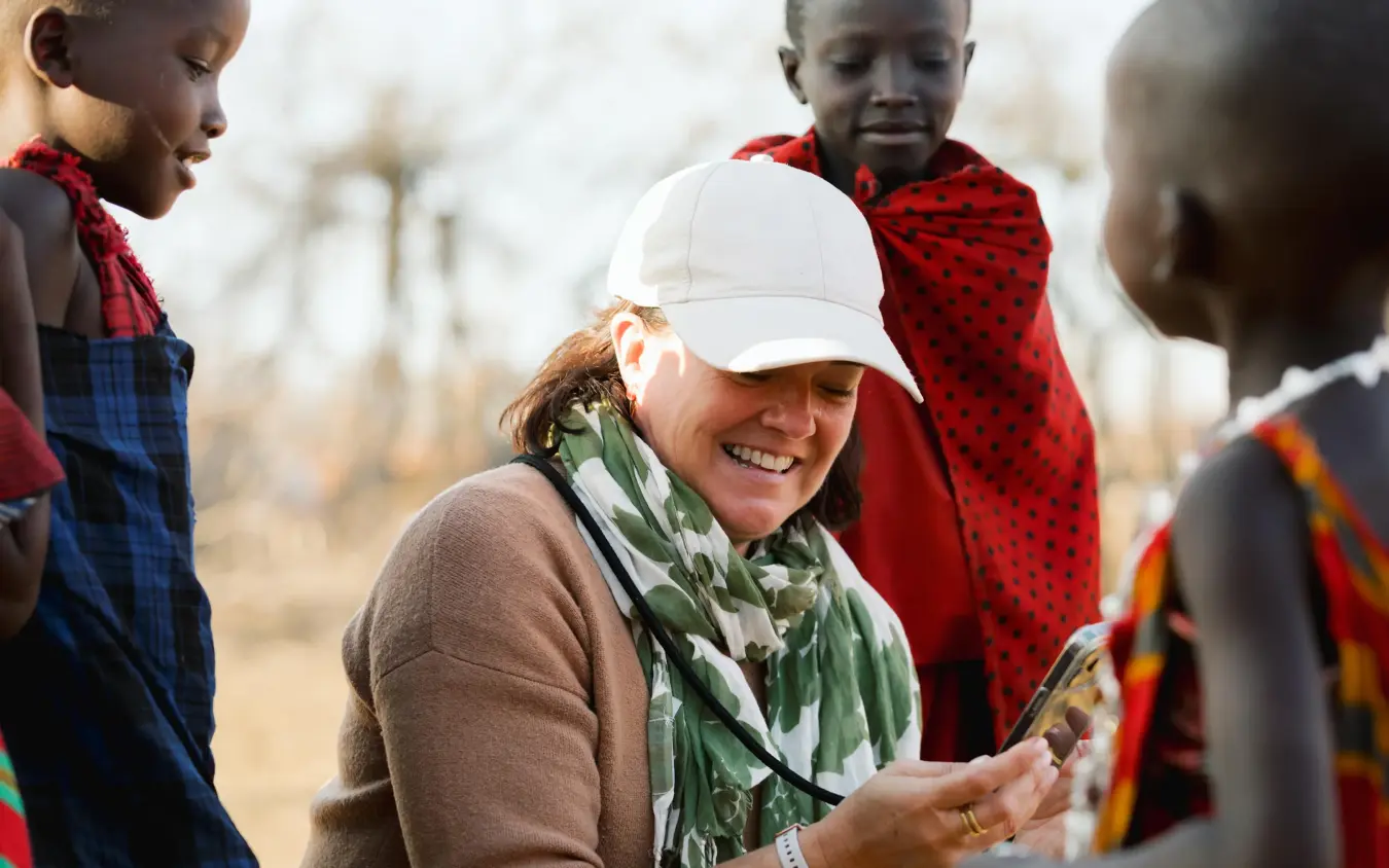 Western tourist interacting with local children in savanna village setting, Olkeri Camp, Tarangire National Park, Tanzania