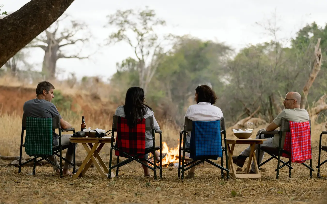 Guests relaxing by campfire in safari camp with woodland backdrop, Olkeri Camp, Tarangire National Park, Tanzania