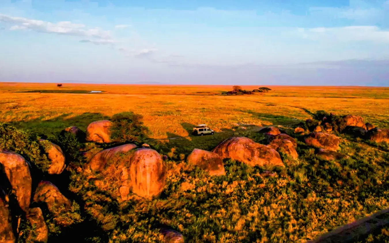 Vast savanna landscape with scattered rock formations and vehicle, Olmara Serengeti, Serengeti National Park, Tanzania
