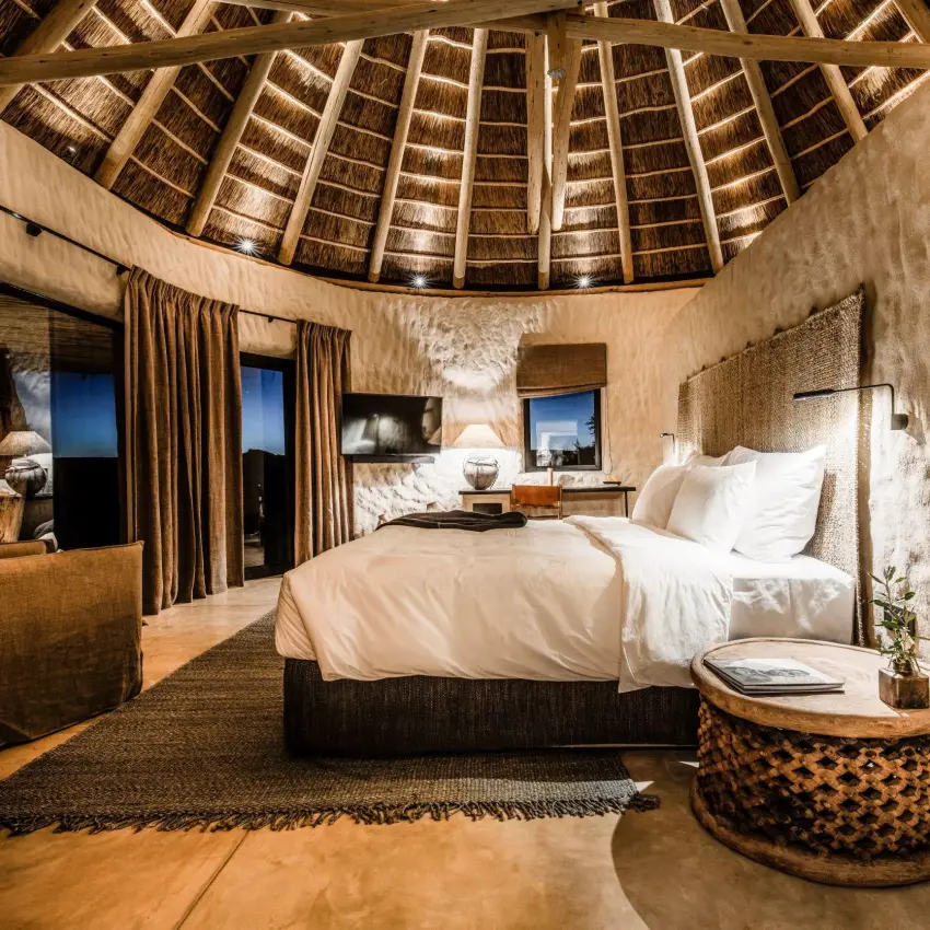 Circular thatched-roof bedroom with white linens and earth tones, Omaanda, Windhoek, Namibia