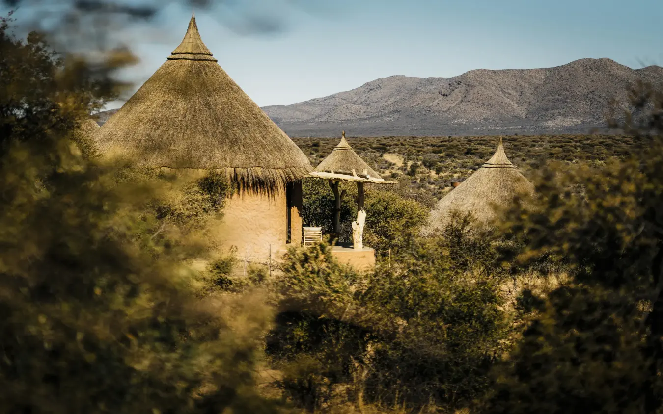 Thatched-roof structures nestled in arid savanna landscape, Omaanda, Windhoek, Namibia