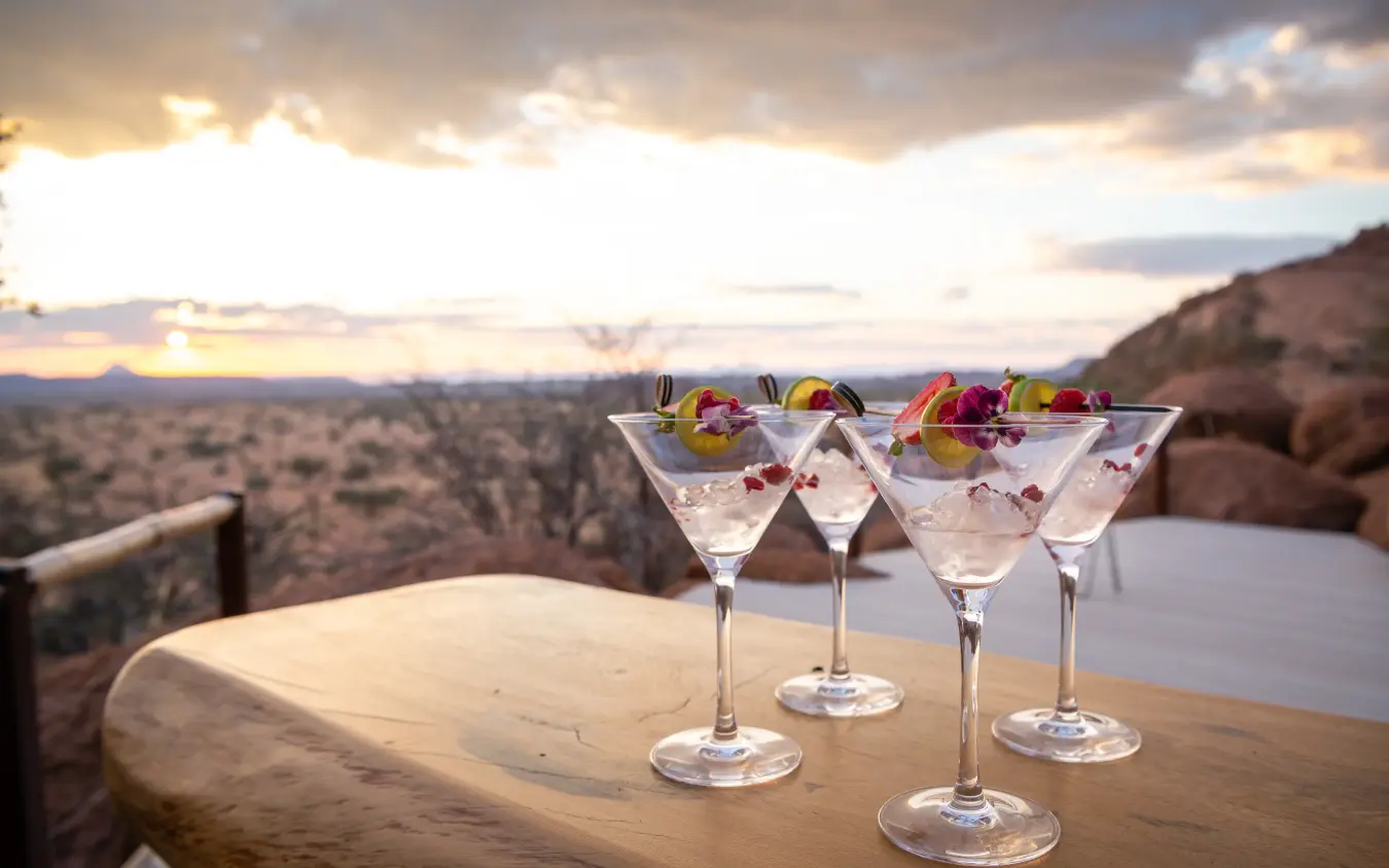 Cocktails on wooden deck overlooking savanna at sunset, Onduli Ridge, Damaraland, Namibia