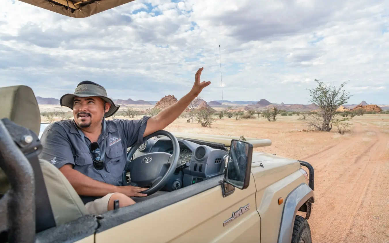 Guide pointing across savanna landscape from open vehicle, Onduli Ridge, Damaraland, Namibia