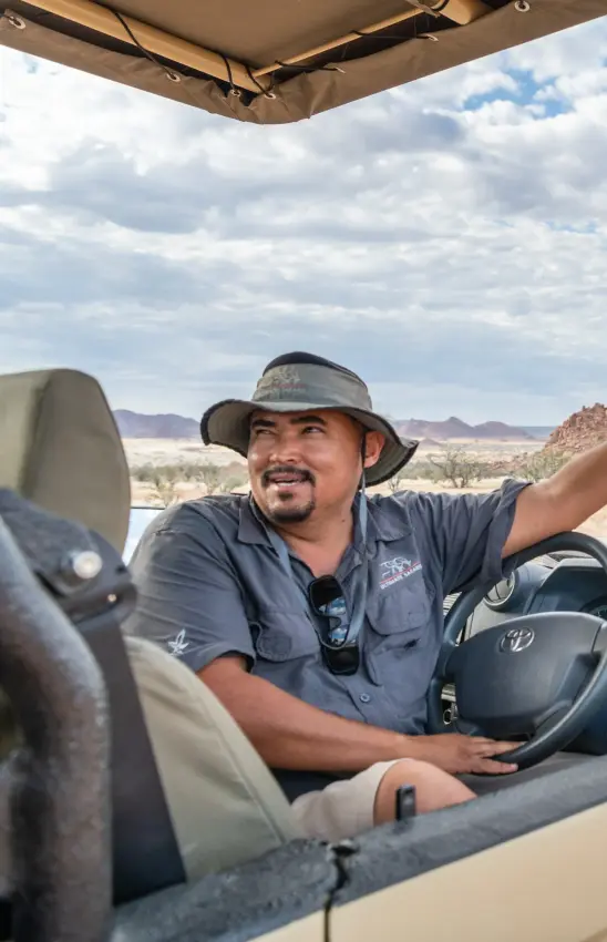 Guide pointing across savanna landscape from open vehicle, Onduli Ridge, Damaraland, Namibia