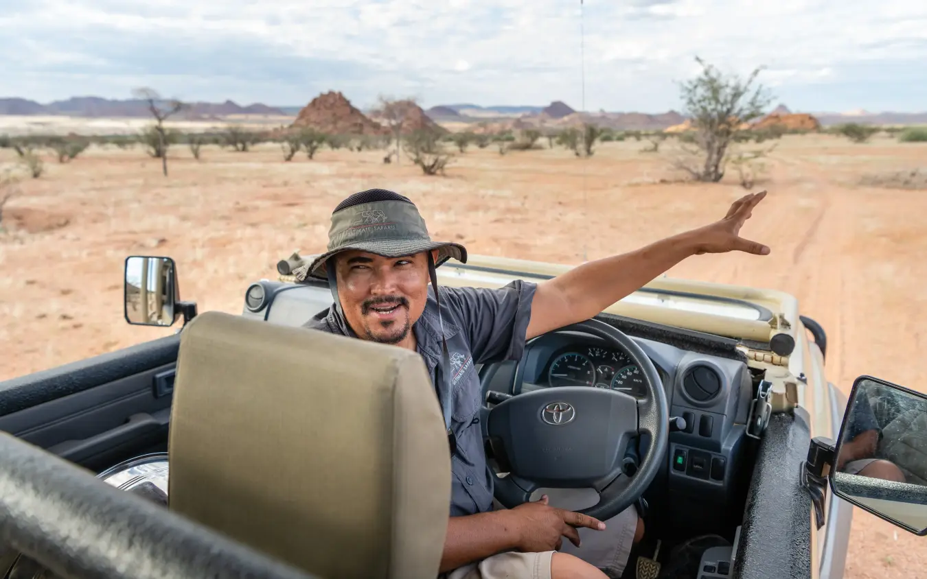 Man in open vehicle on red dirt road through savanna, Namibia