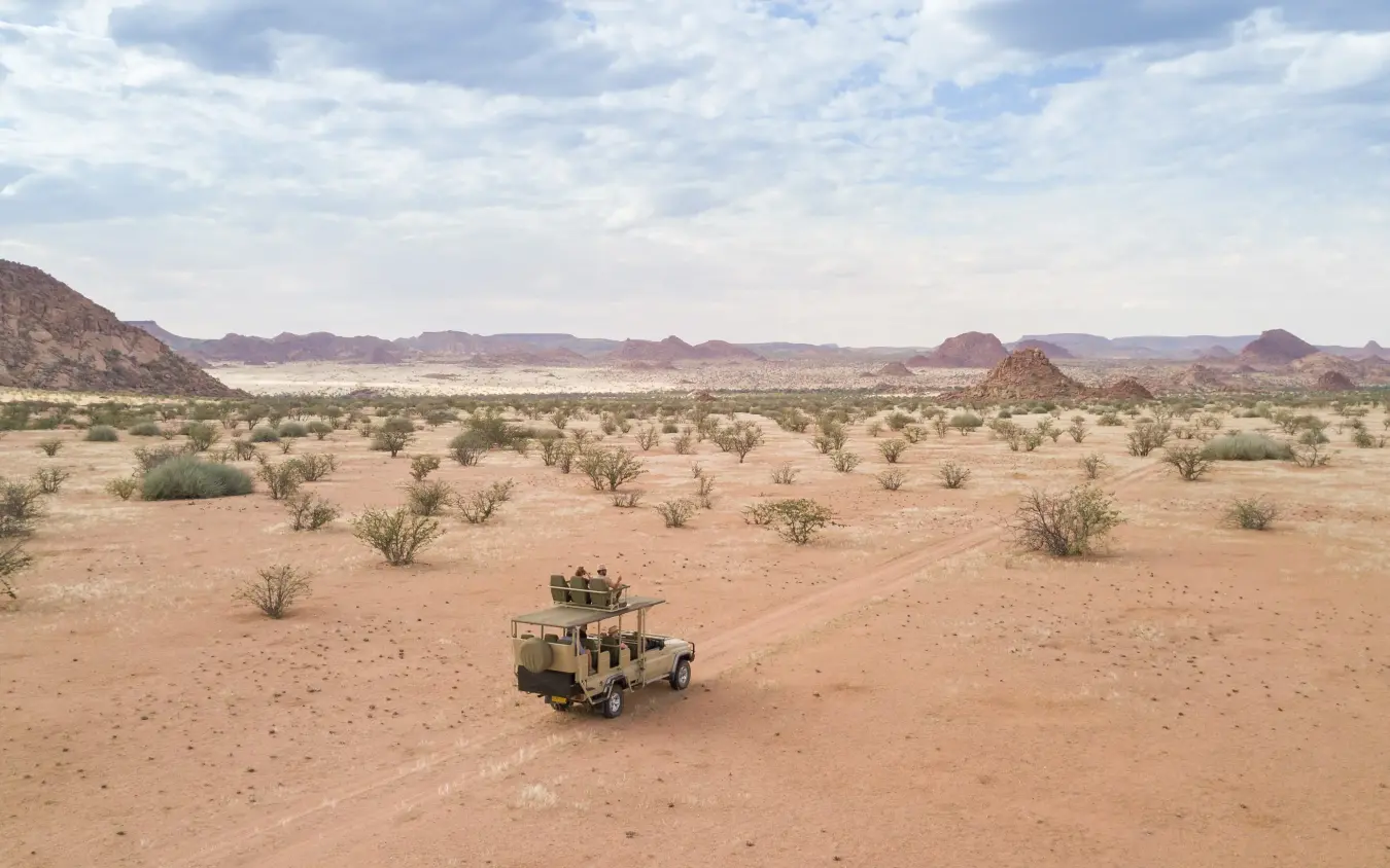 Safari vehicle driving through sparse desert landscape with mountains, Onduli Ridge, Damaraland, Namibia