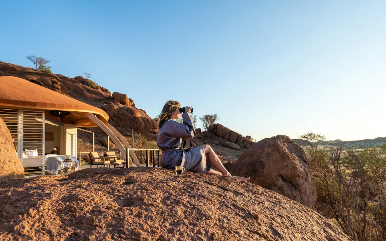 Guest relaxing on rocky outcrop near lodge at sunset, Onduli Ridge, Damaraland, Namibia
