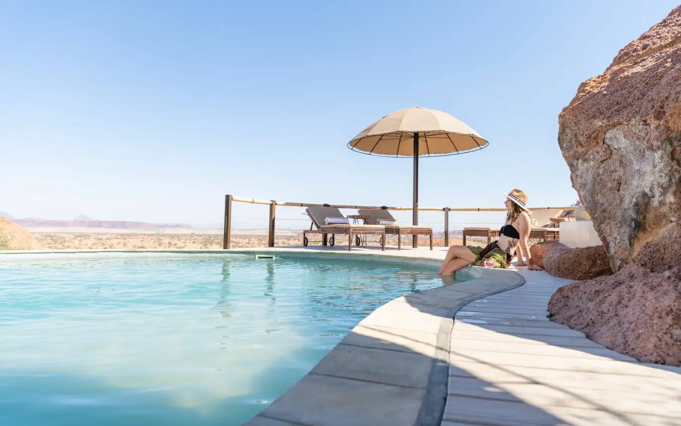 Infinity pool overlooking desert landscape with loungers and umbrella, Onduli Ridge, Damaraland, Namibia