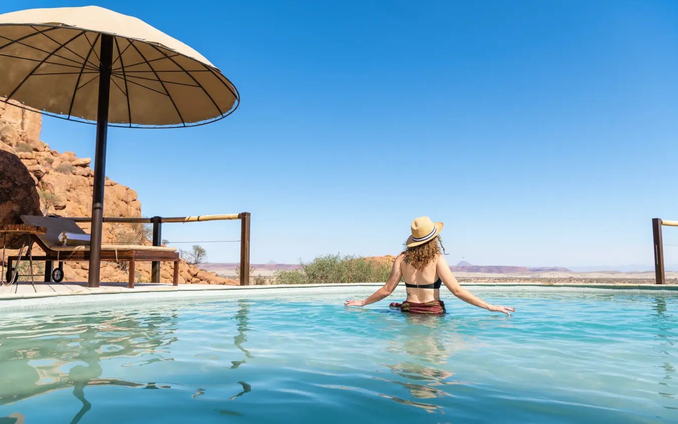 Woman relaxing in infinity pool overlooking desert landscape, Onduli Ridge, Damaraland, Namibia