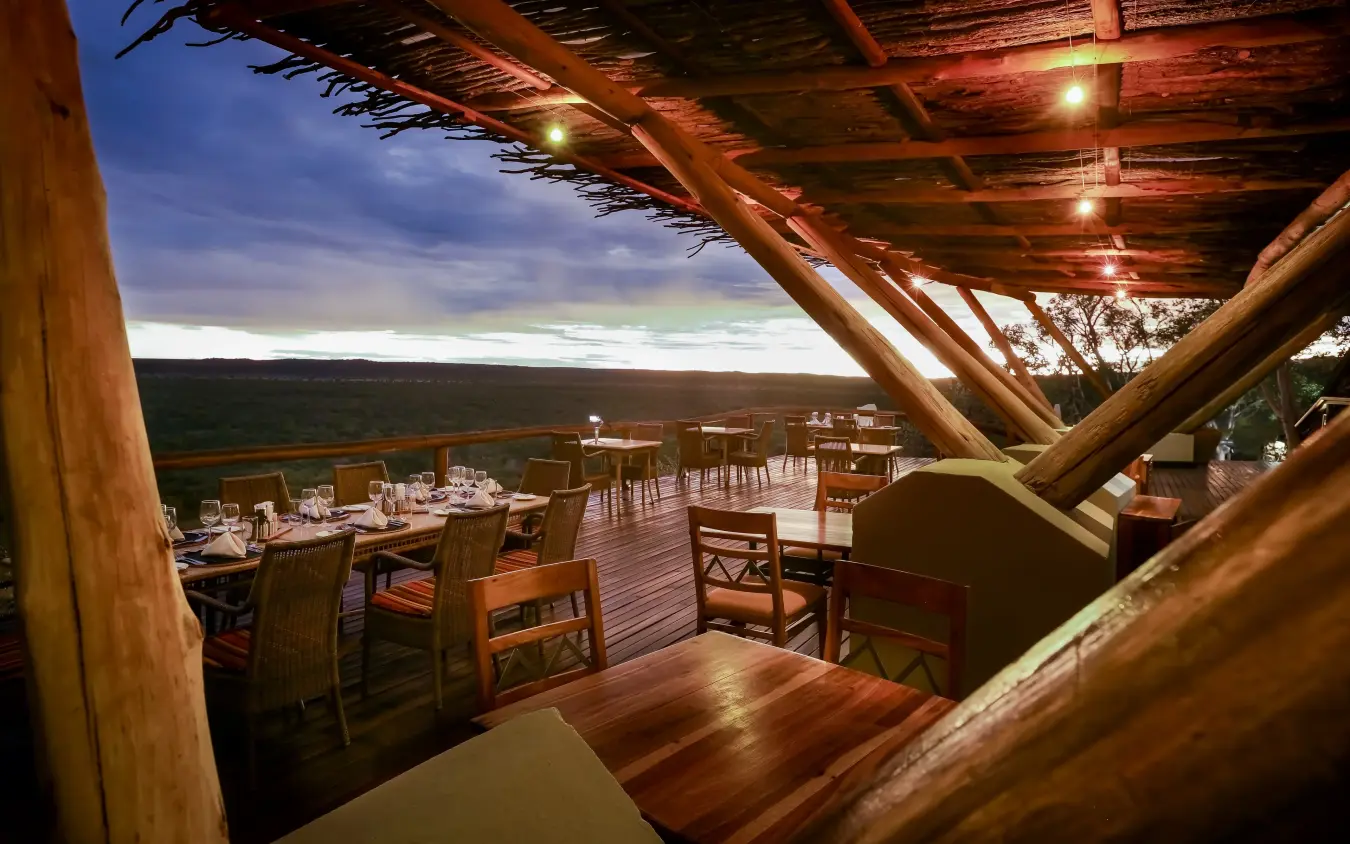 Open-air dining deck with wooden beams overlooking vast savanna landscape at dusk, Ongava Lodge, Etosha National Park, Namibia