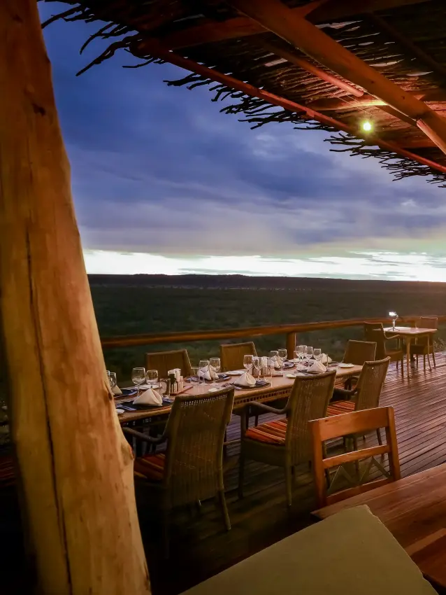 Open-air dining deck with wooden beams overlooking vast savanna landscape at dusk, Ongava Lodge, Etosha National Park, Namibia