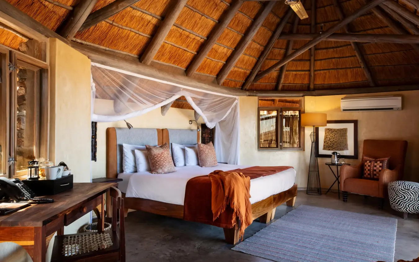 Luxury safari lodge bedroom with thatched roof and canopied bed, Ongava Lodge, Etosha National Park, Namibia