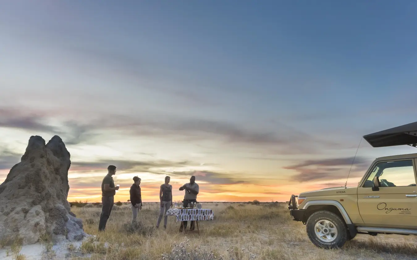 Safari vehicle with guests at sunset in arid grassland with rock formation, Onguma Camp Kala, Etosha National Park, Namibia