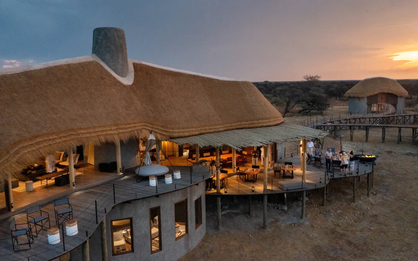 Thatched lodge with wooden deck overlooking waterhole at dusk, Onguma Camp Kala, Etosha National Park, Namibia