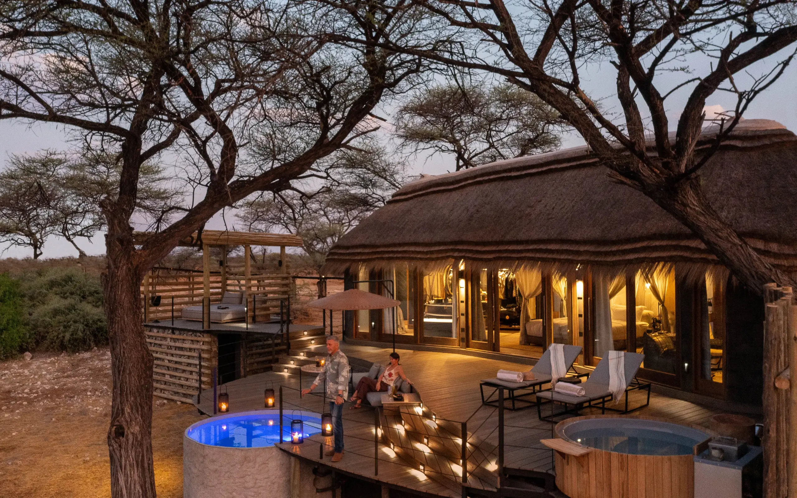 Luxury lodge deck with infinity pools and hot tub under acacia trees at dusk, Onguma Camp Kala, Etosha National Park, Namibia