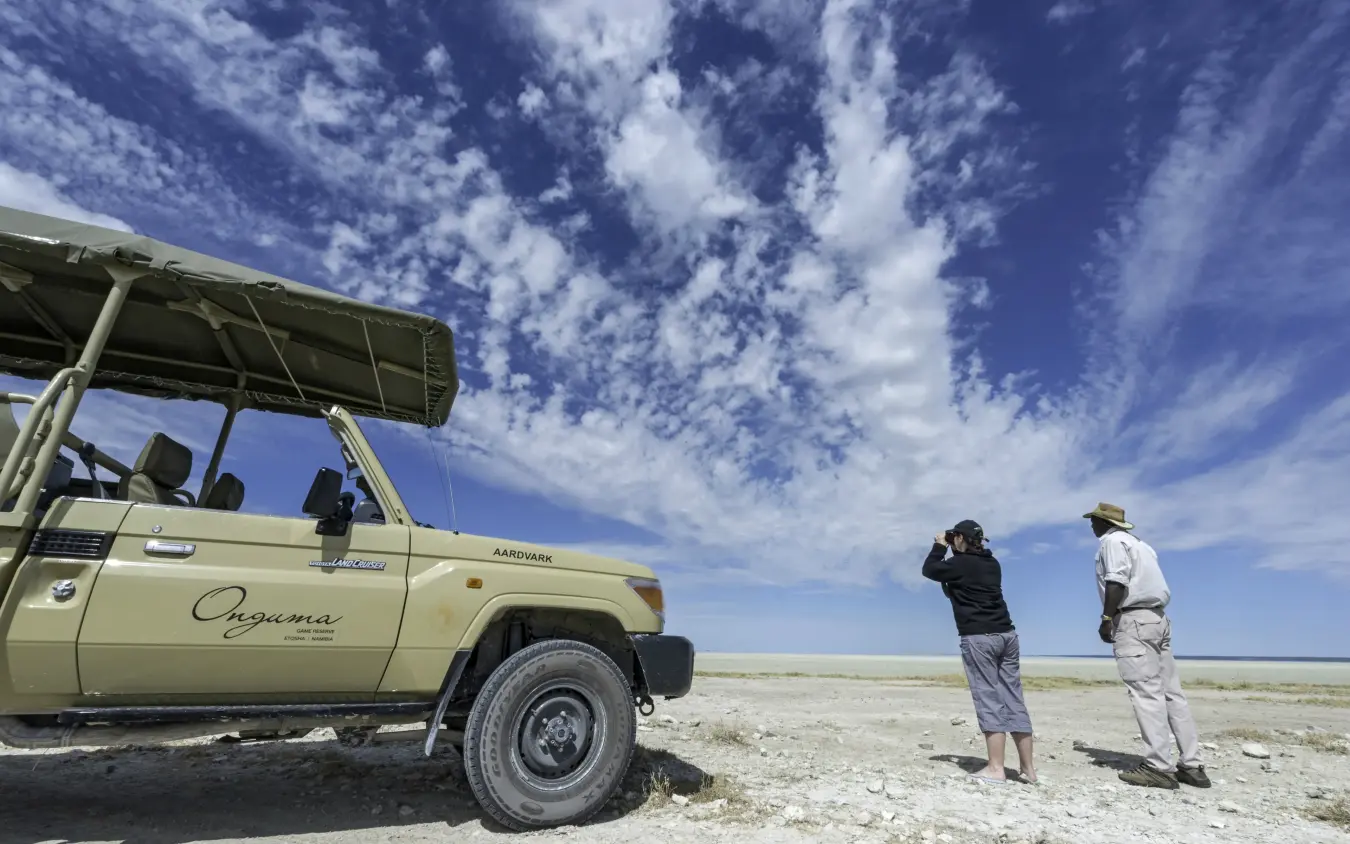 Safari vehicle with guests wildlife spotting on vast salt pan landscape, Onguma Tented Camp, Etosha National Park, Namibia