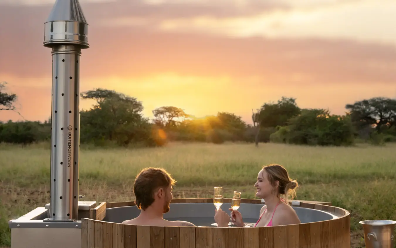 Couple bathing in wooden hot tub at sunset overlooking savanna grassland, Onguma Trails Camp, Etosha National Park, Namibia