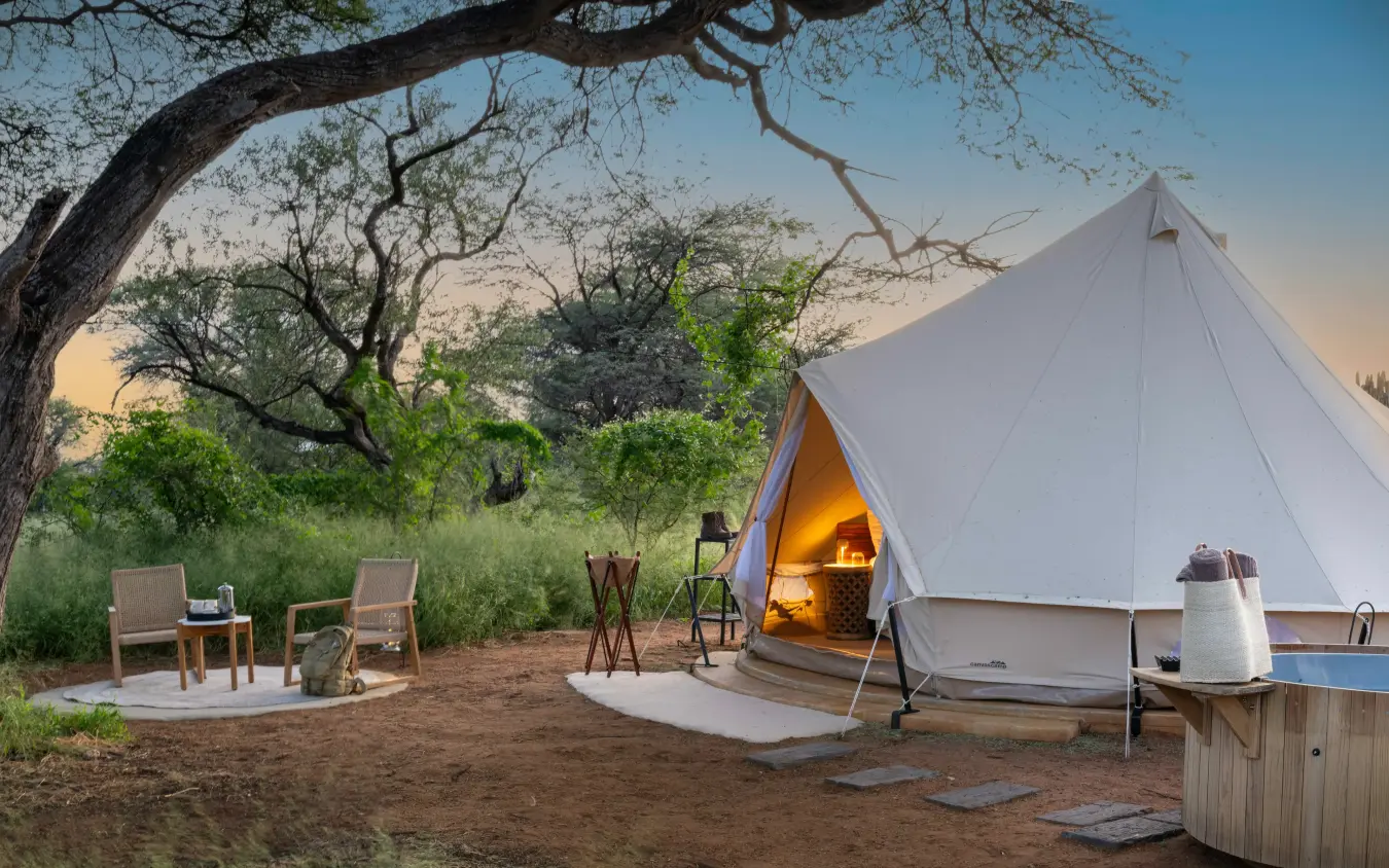 Luxury bell tent with warm interior lighting at dusk in savanna setting, Onguma Trails Camp, Etosha National Park, Namibia
