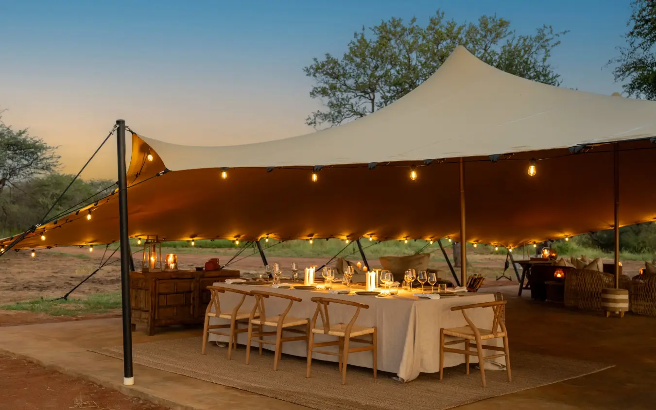 Outdoor dining tent with table settings at dusk in savanna landscape, Onguma Trails Camp, Etosha National Park, Namibia