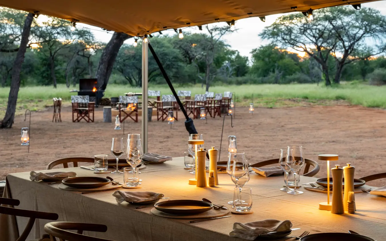 Outdoor dining table set under canvas canopy in savanna landscape at dusk, Onguma Trails Camp, Etosha National Park, Namibia