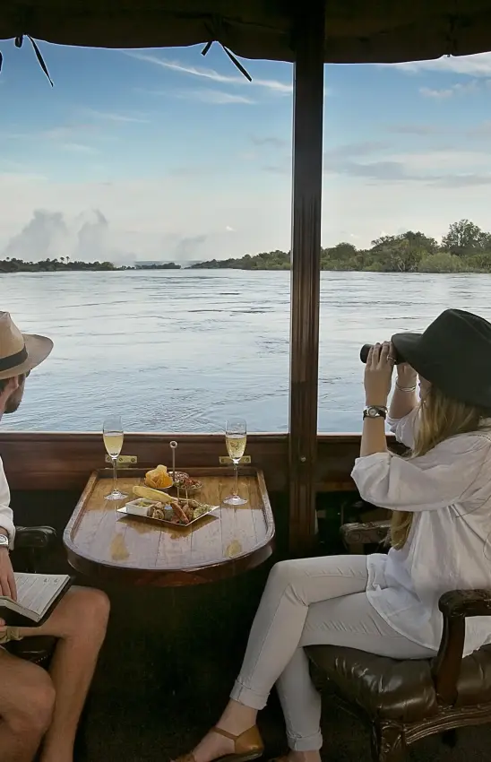 Guests viewing river from covered boat deck with refreshments, Palm River Hotel, Victoria Falls, Zimbabwe