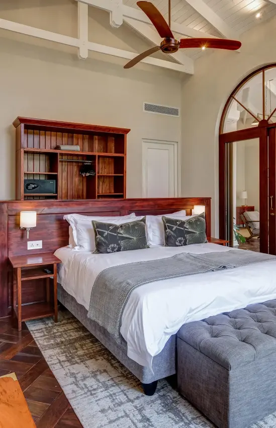 Spacious bedroom with wooden furnishings and arched mirror, Palm River Hotel, Victoria Falls, Zimbabwe