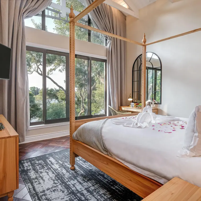 Bedroom with wooden four-poster bed and large windows, Palm River Hotel, Victoria Falls, Zimbabwe
