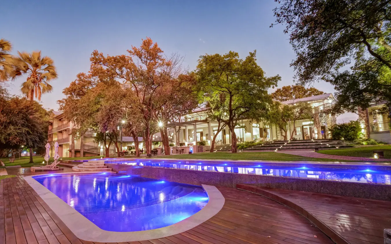 Illuminated swimming pool at dusk with manicured grounds, Palm River Hotel, Victoria Falls, Zimbabwe