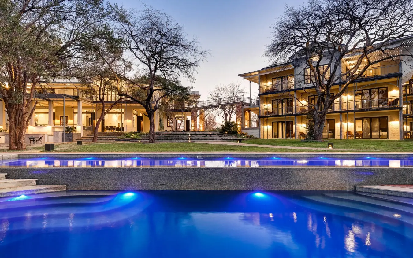 Illuminated swimming pool with modern lodge buildings at dusk, Palm River Hotel, Victoria Falls, Zimbabwe
