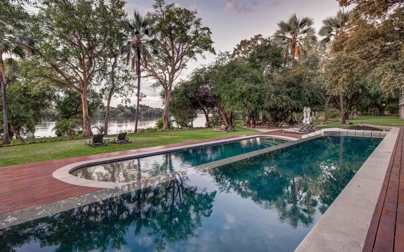 Resort swimming pool overlooking river with mature trees, Palm River Hotel, Victoria Falls, Zimbabwe